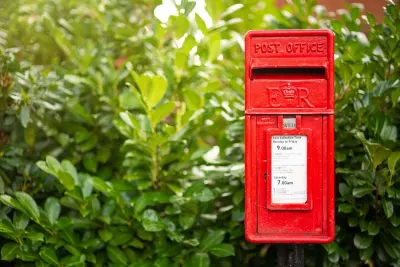 A traditional red British Post Office postbox beside a green hedge