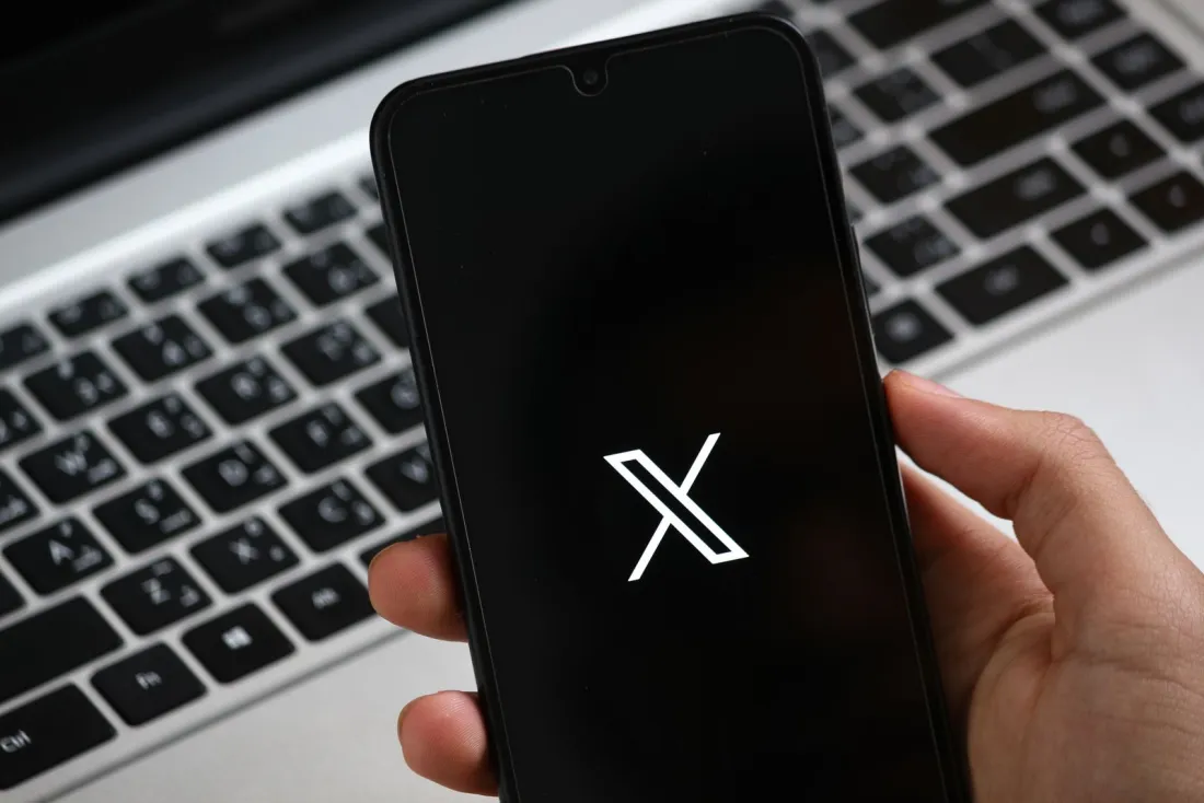 Hand holding a smartphone showing the X logo, illustrating the blue checkmark at the centre of why the European Commission is fining X