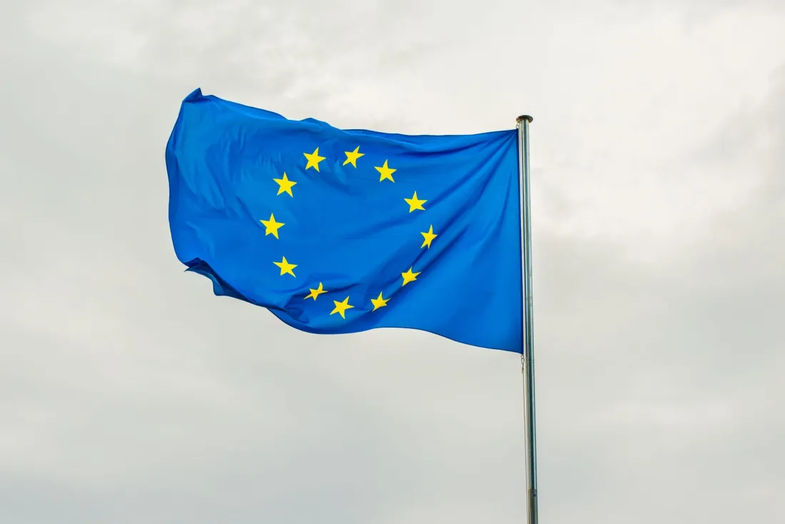 European Union flag flying against a grey sky, representing the EU blocking statute and its conflict with US secondary sanctions on Iran