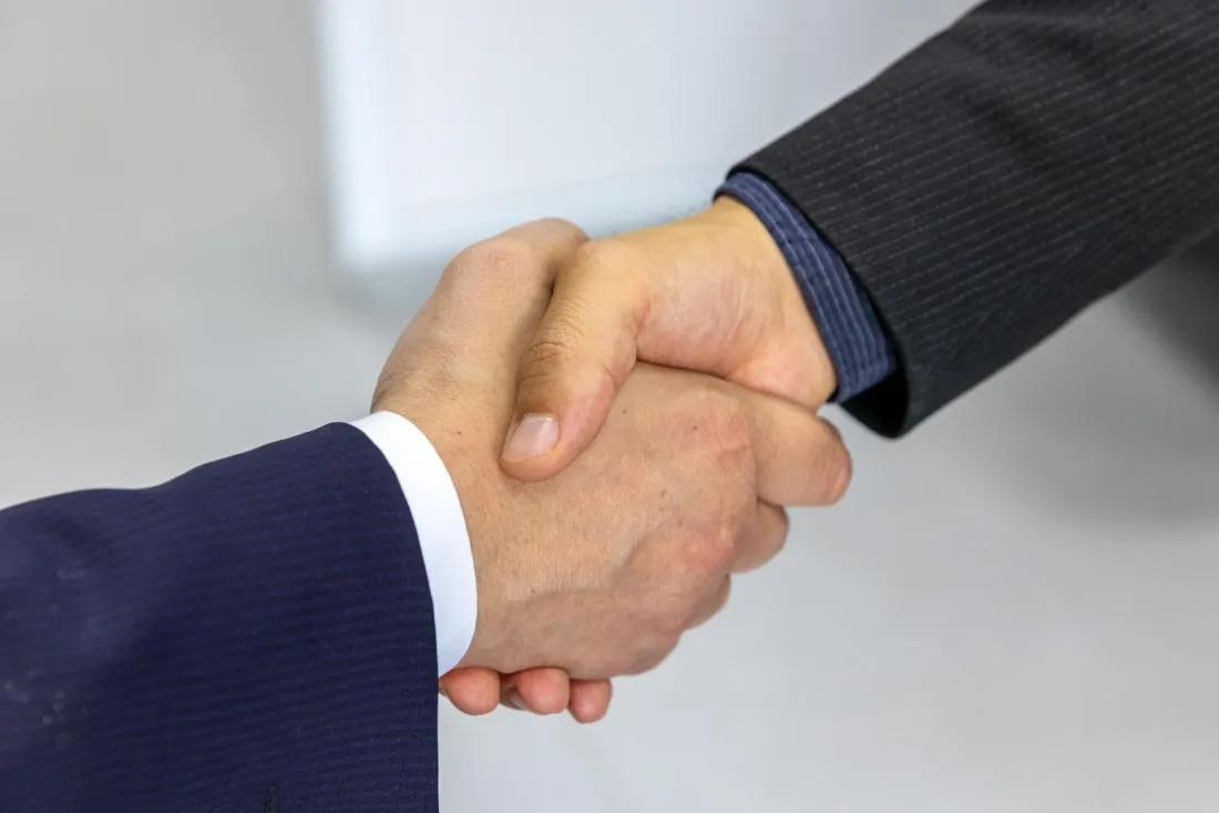 Two business people shaking hands, illustrating FRAND licensing negotiations and the unwilling licensee test in UPC patent litigation