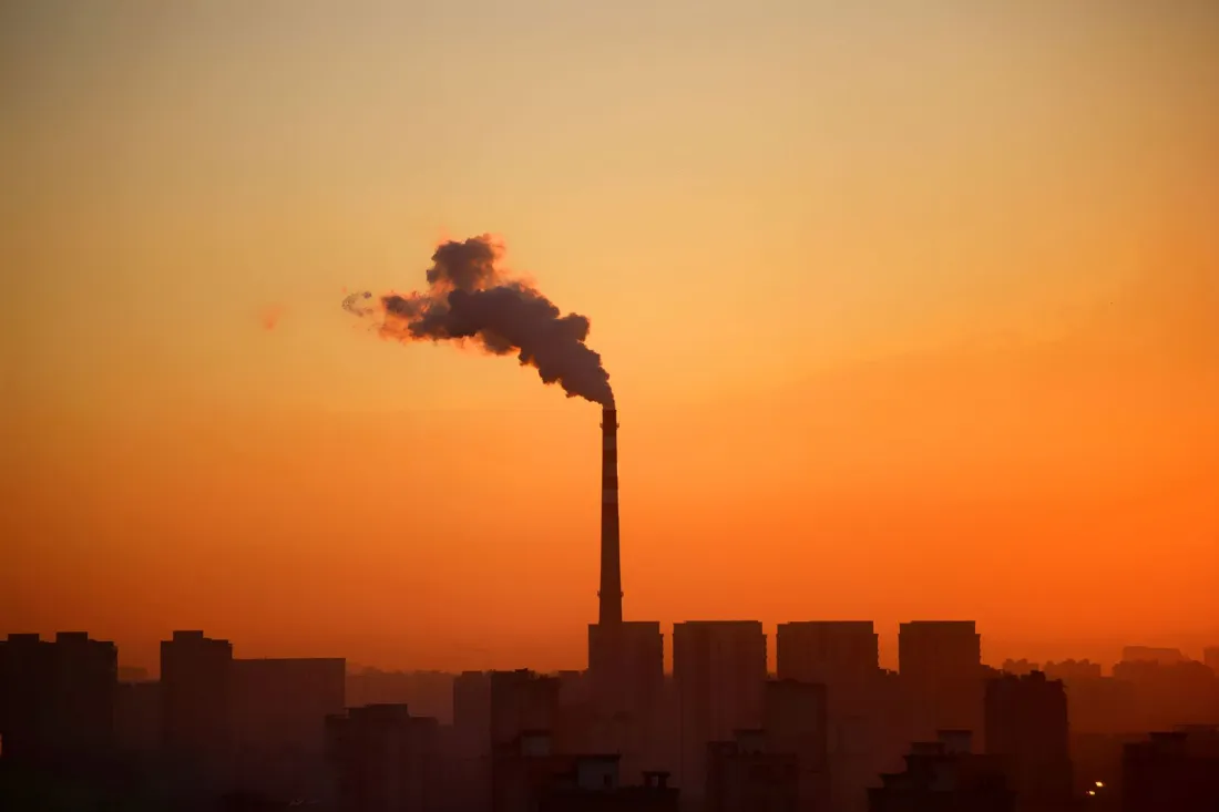 Industrial smokestack emitting smoke against an orange sunset sky, illustrating net zero targets and the future performance rules in the Empowering Consumers Directive