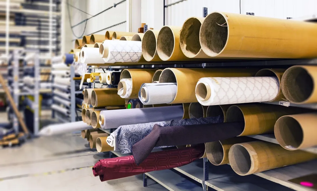 Rolls of textile fabric stacked on racks in a factory warehouse, illustrating supply chains, CSRD after the Omnibus and what the Empowering Consumers Directive means for product claims