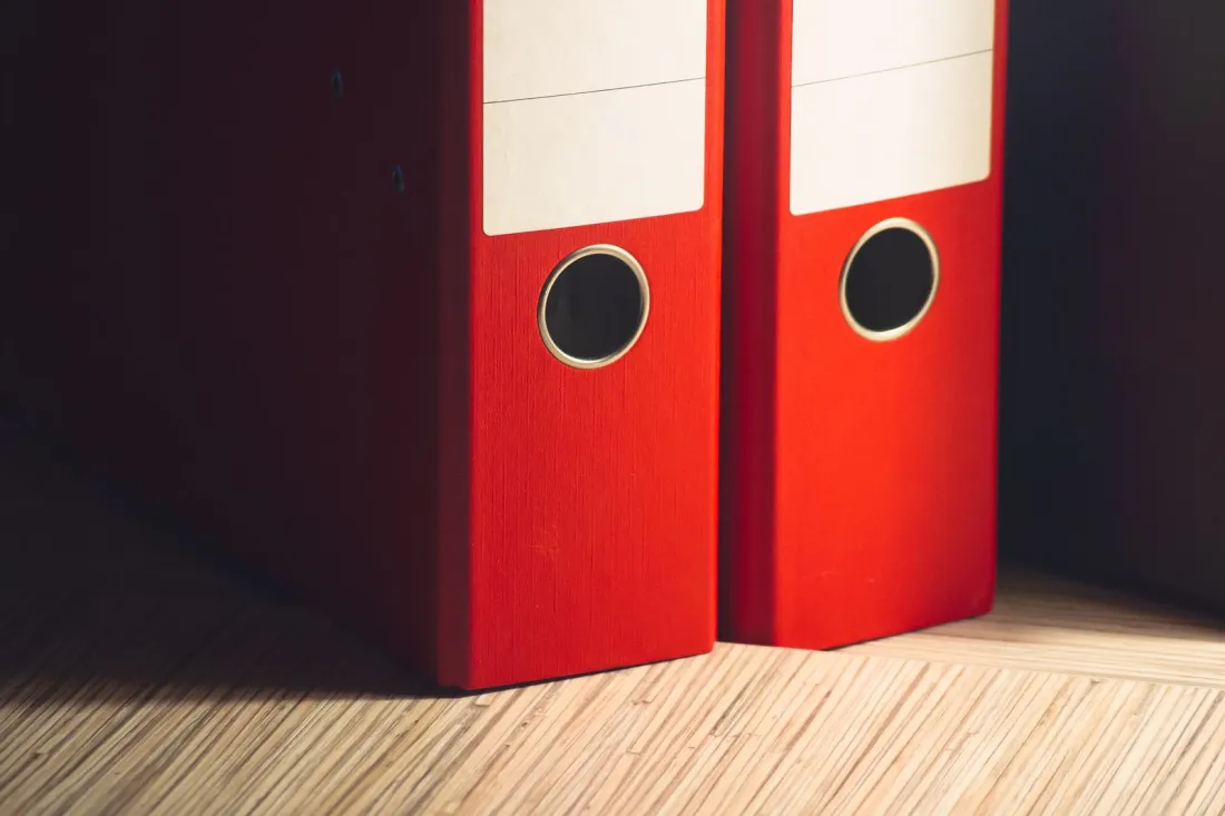 Two red lever arch files on a desk, illustrating the pay and HR records that California pay data reporting puts in front of the regulator