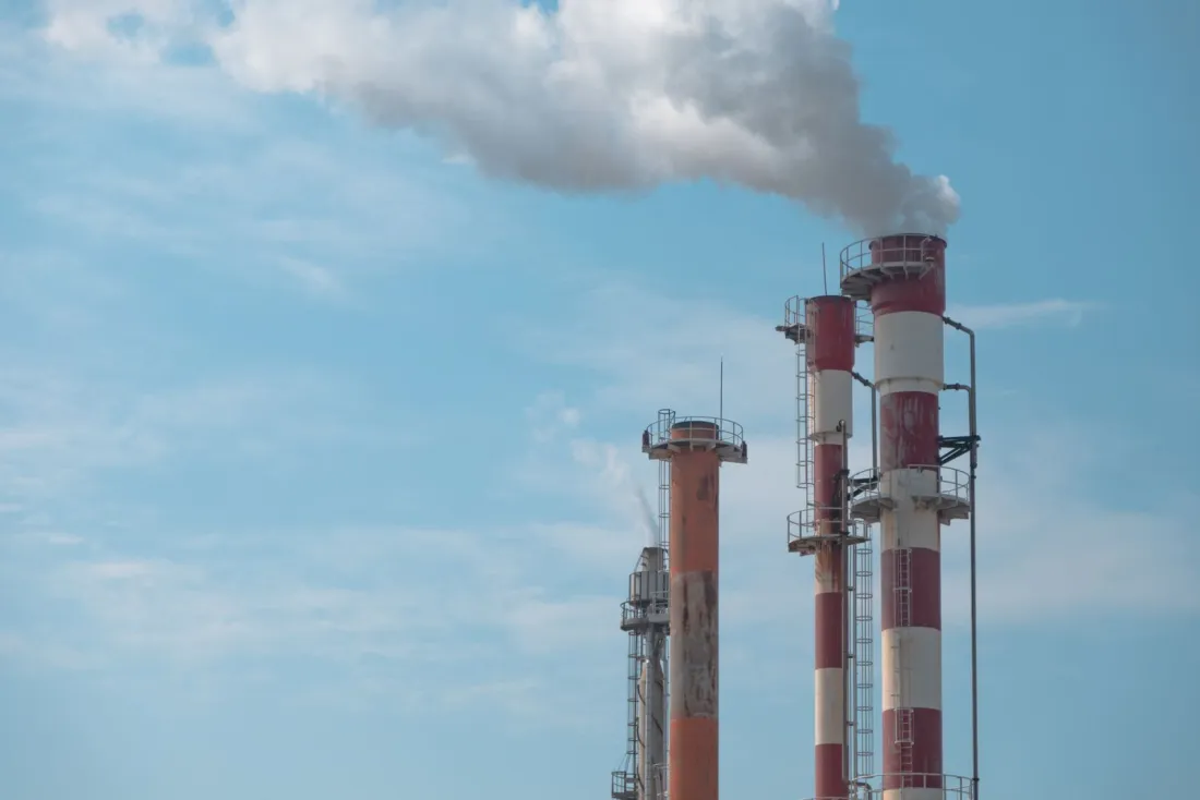 Industrial smokestacks releasing emissions into a blue sky, illustrating Clean Air Act preemption arguments in Suncor v Boulder