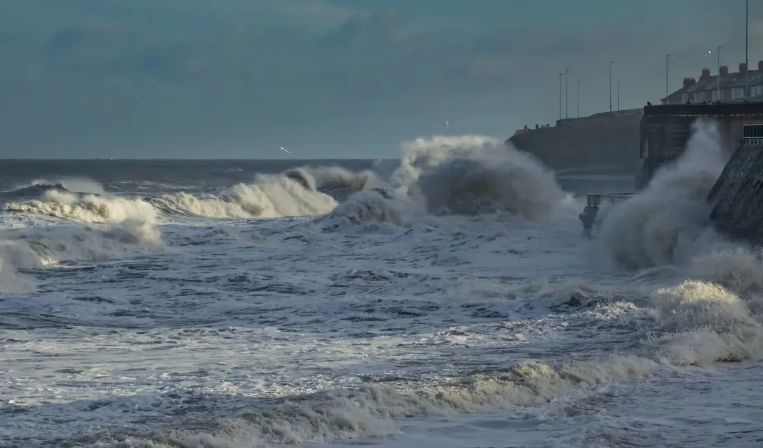 Storm waves crashing against a coastal sea wall, illustrating the coastal and sea-level harms behind climate change lawsuits against oil companies