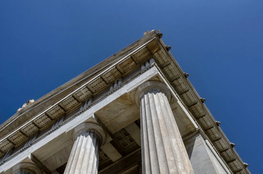 Low-angle view of neoclassical courthouse columns against a blue sky, representing the US court rulings on whether prediction markets are legal