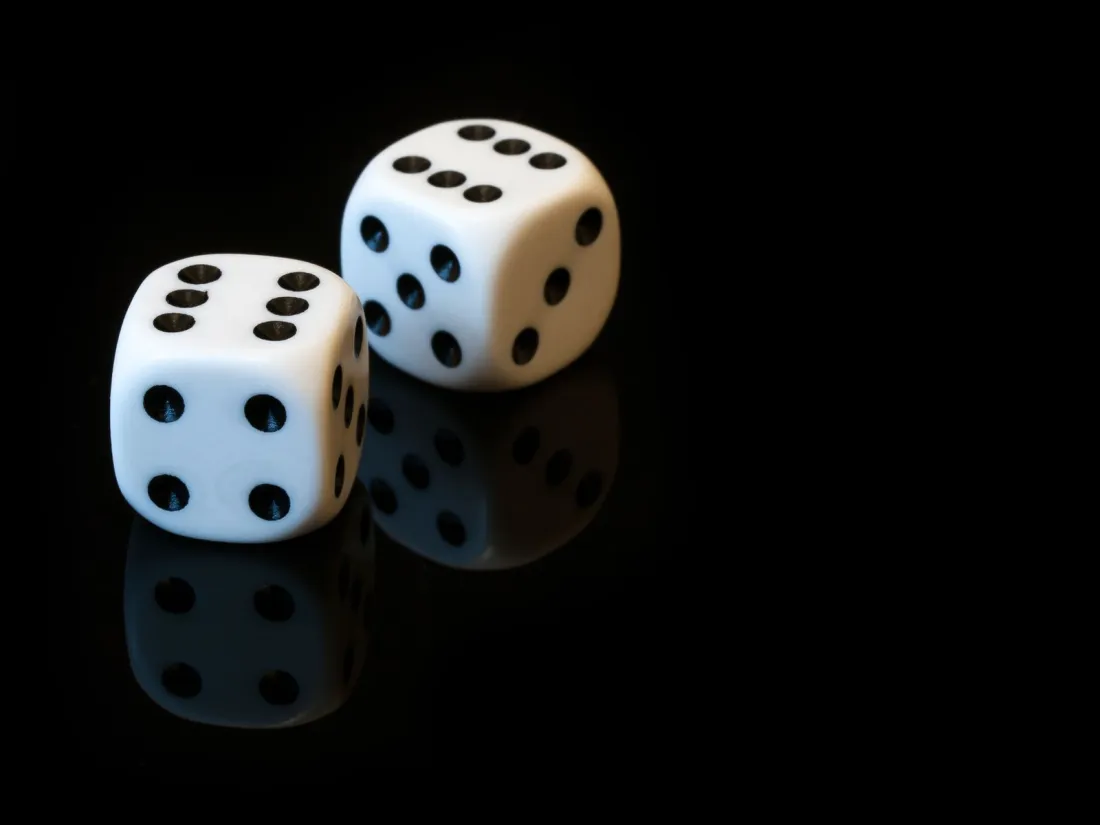 Two white dice on a black reflective surface, illustrating UK and European gambling law on prediction markets