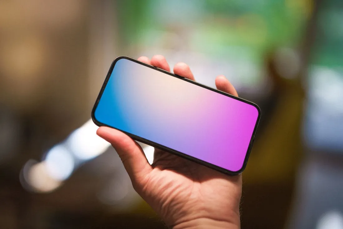 Hand holding a smartphone with a blank gradient screen, illustrating the Google Play Store class action lawsuit