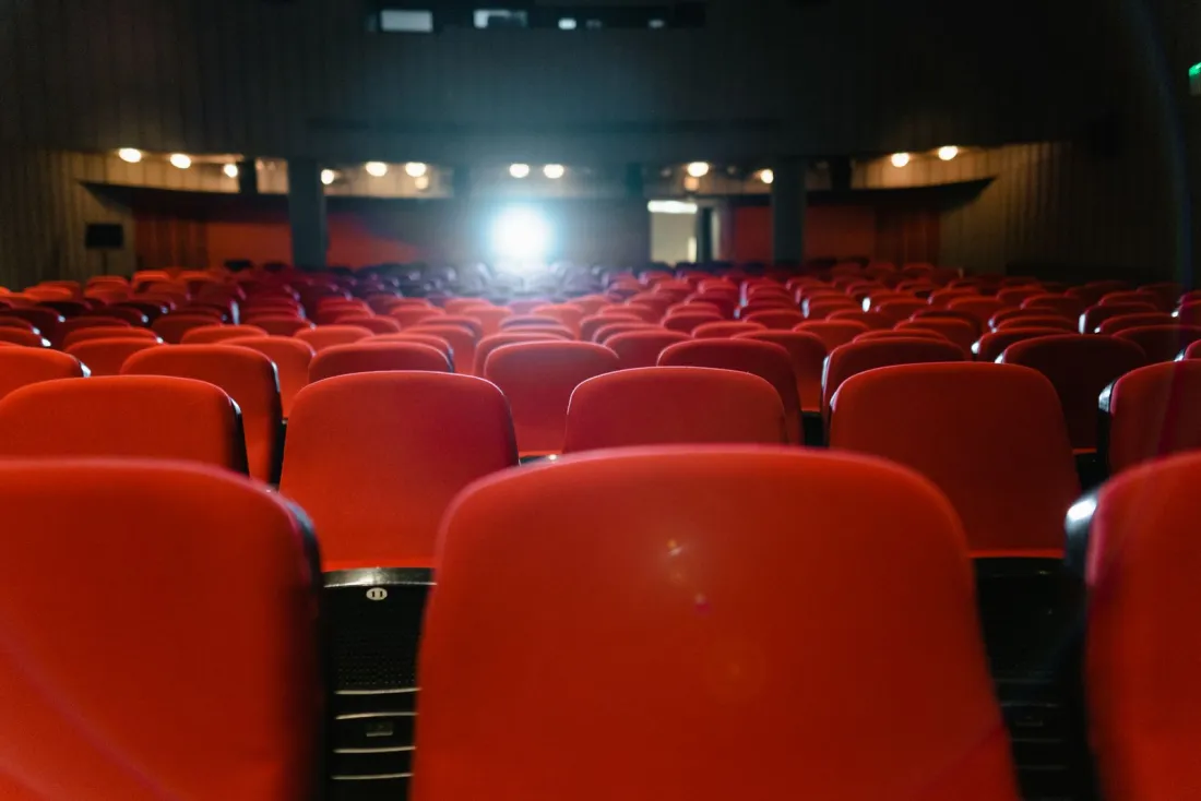 Rows of empty red cinema seats facing a lit screen, illustrating the theatrical release commitments in the Paramount Warner Bros merger settlement