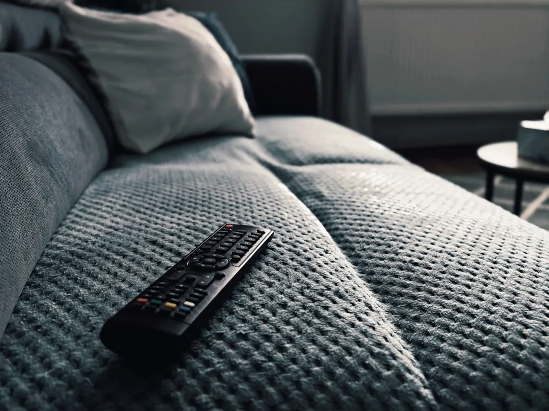 Television remote control resting on a grey sofa, illustrating what happens to HBO Max and Paramount+ after the Warner Bros Paramount merger
