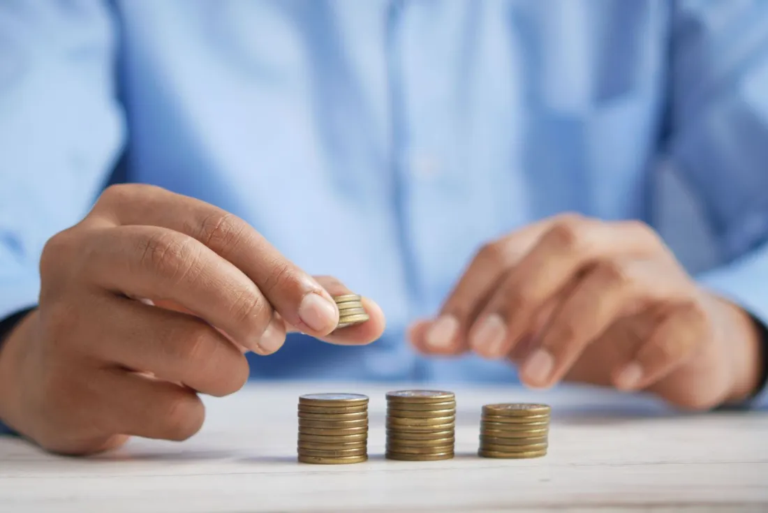 Hands stacking gold coins on a desk, illustrating the Vanuatu citizenship by investment cost and government contribution