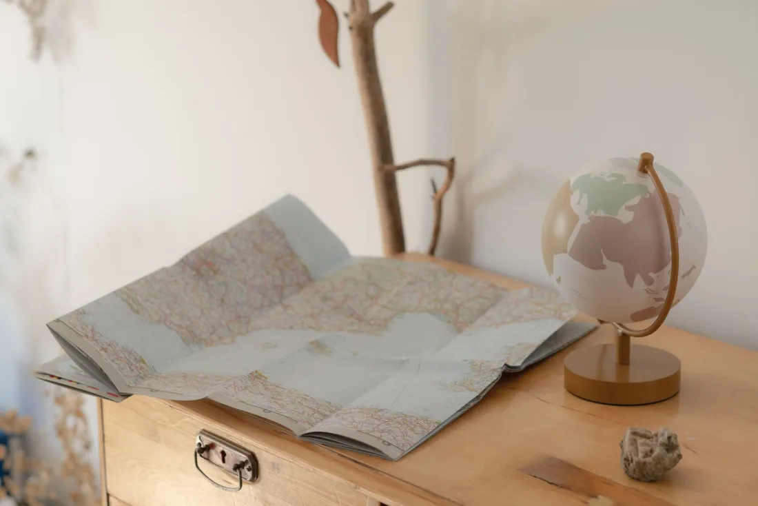 Folded road map and a small globe on a wooden chest, illustrating jurisdiction choices in an international divorce