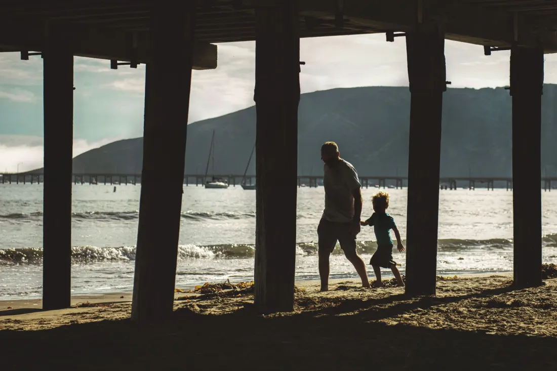 Silhouette of a parent and young child walking on a beach beneath a pier, illustrating children in a cross border divorce
