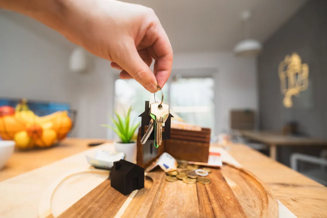 Hand holding a set of house keys over a wooden table with a small model house, illustrating whether foreigners can buy property abroad