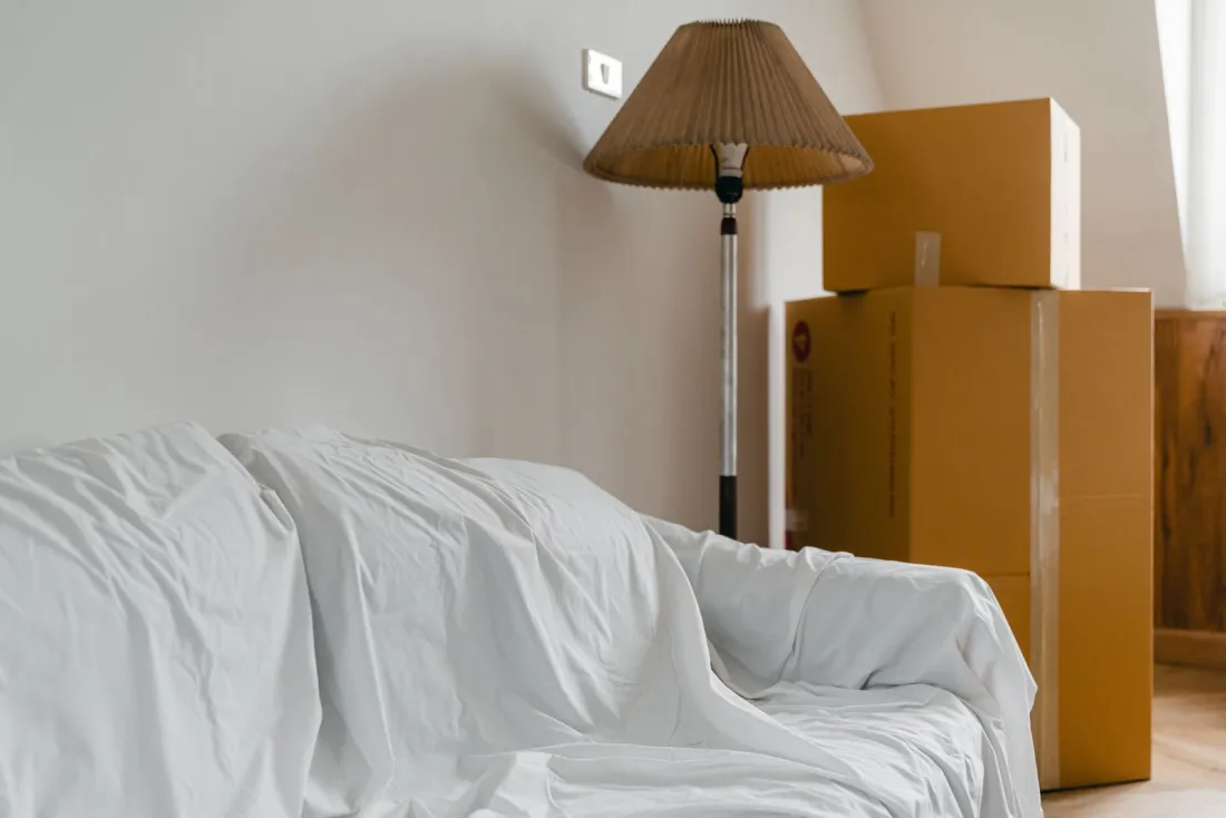 Sofa under a dust sheet beside stacked delivery boxes, illustrating the delivery extras at the centre of the CMA fines on Appliances Direct and Wayfair