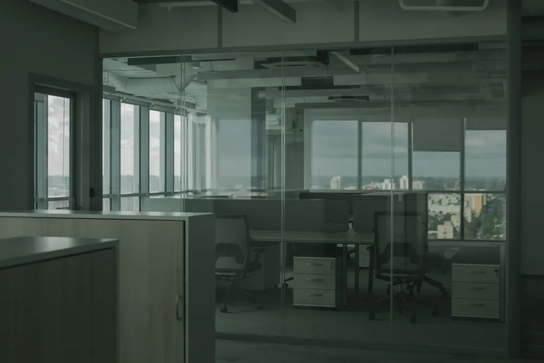 Glass-walled office with empty desks and a city view, illustrating a UK Expansion Worker licence for an overseas company setting up in the UK
