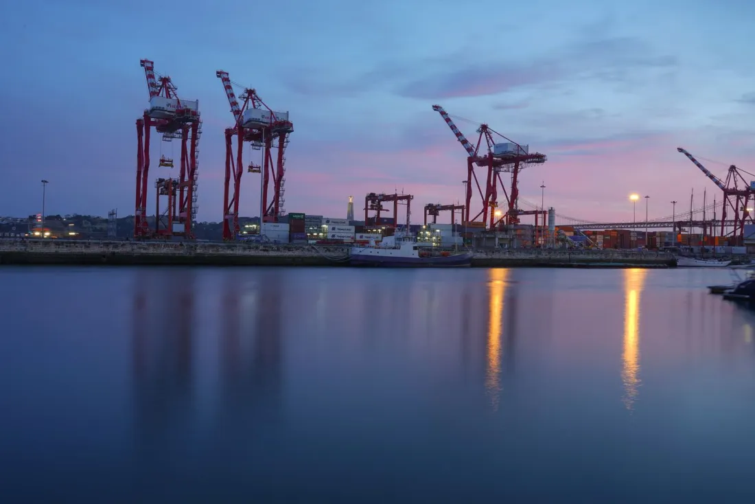 Container cranes silhouetted against a dusk sky over a harbour, illustrating the cross-border payments in the Bank of America OFAC sanctions settlement