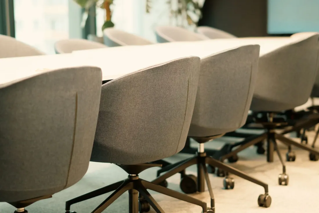 Row of empty grey swivel chairs around a long meeting table, illustrating the 30 October 2026 sexual harassment and third-party harassment duties for employers
