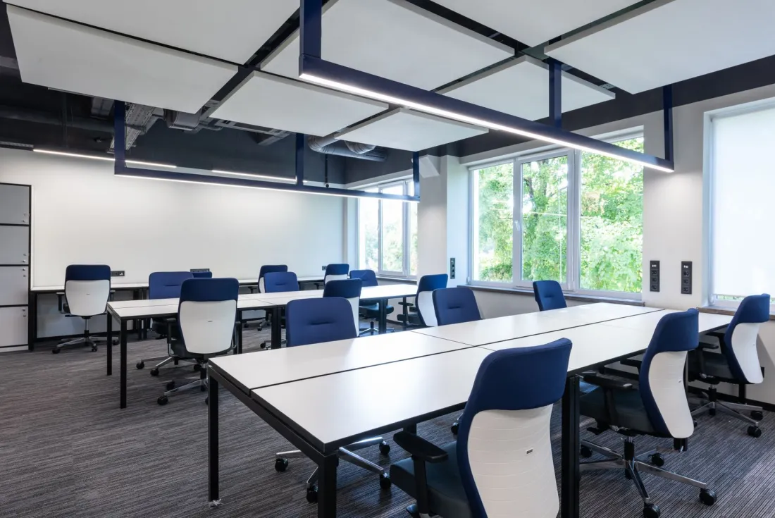 Empty open-plan office with white desks and blue chairs beside tall windows, illustrating an overseas group preparing its UK workforce for the Employment Rights Act changes