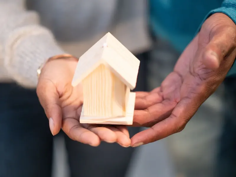 Hands holding a small wooden model house: family & private client lawyers and advisers