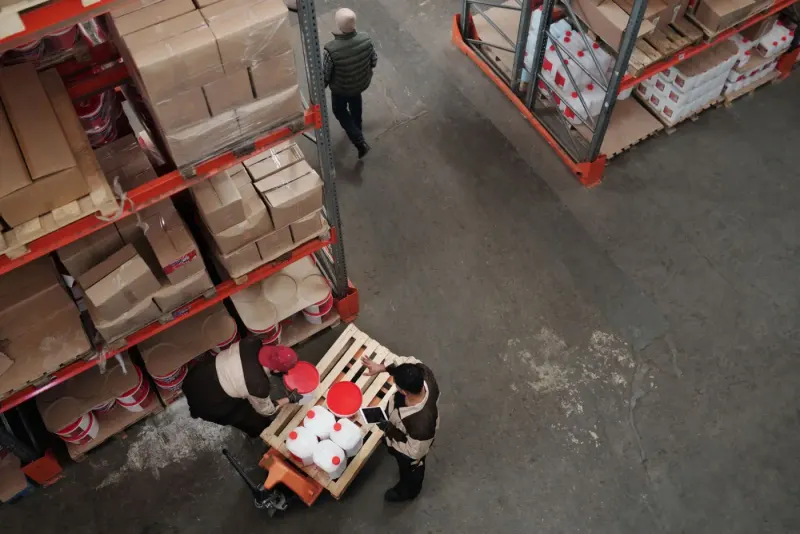 High-angle view of warehouse workers handling stock between shelves: employment & labour lawyers and advisers