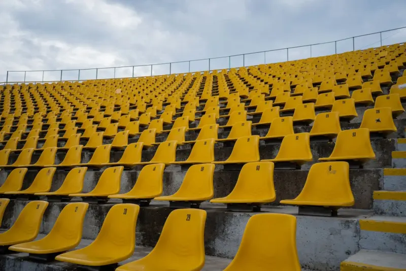 Rows of empty yellow stadium seats on a cloudy day: sports & entertainment lawyers and advisers