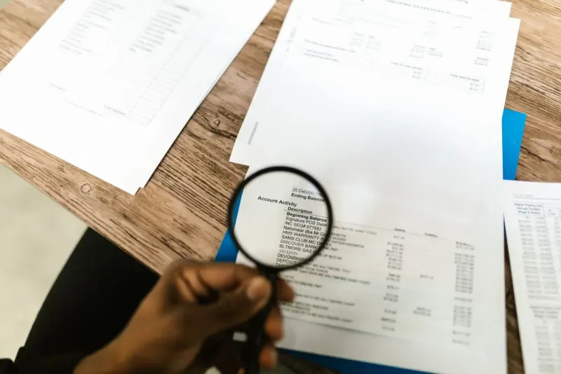 Hand using a magnifying glass to review financial documents: full service accountancy experts and advisers