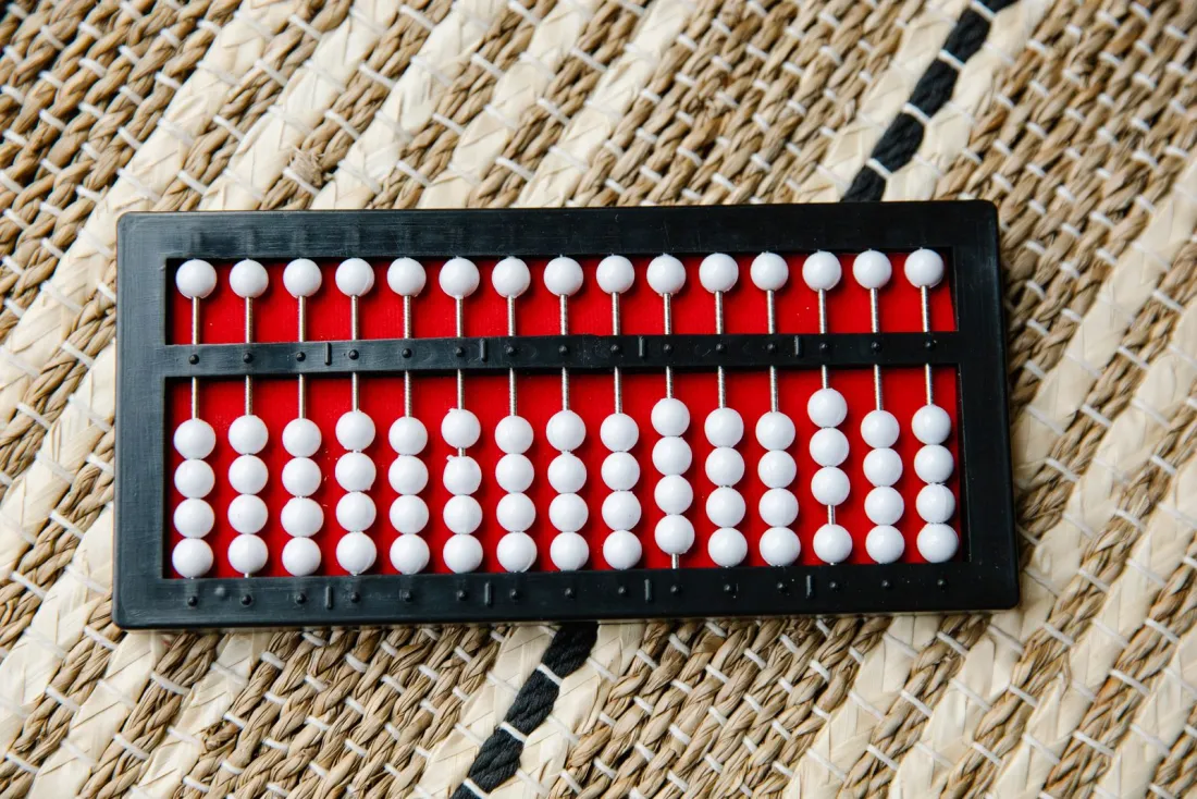 Black abacus with white beads on a woven mat, representing international patent cost and PCT fees in 2026