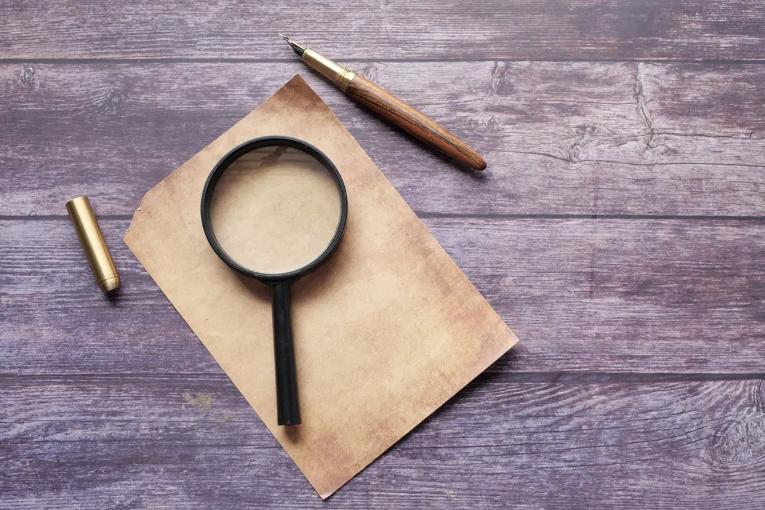 Magnifying glass and fountain pen on paper, representing checks on FCA registered financial advisers before choosing a wealth manager