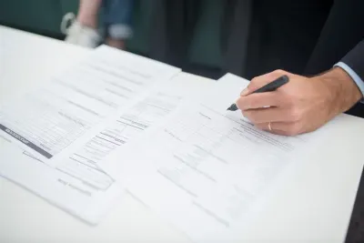 Hand signing insurance documents at a desk, illustrating the choice between claims made vs occurrence policies