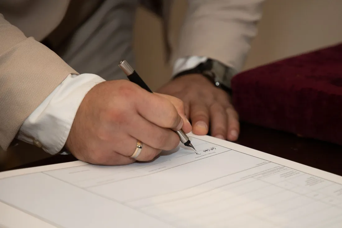 Man wearing a wedding ring signing a postnuptial agreement, illustrating whether prenups and postnups are legally binding in the UK