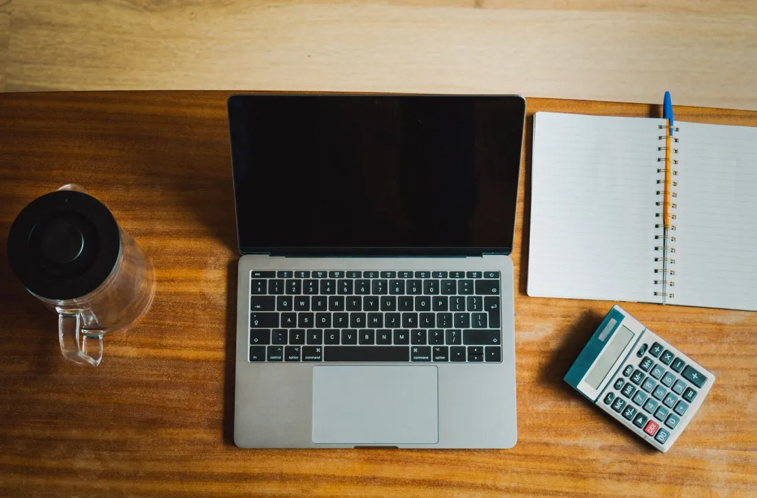 Laptop, notebook and calculator on a wooden desk seen from above, illustrating choosing an international accountant