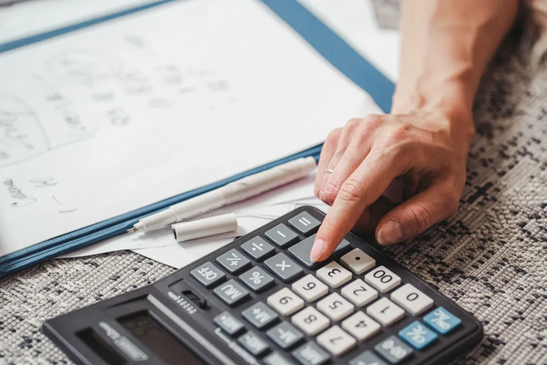Hand pressing a calculator beside client papers, illustrating how to check if an accountant is qualified