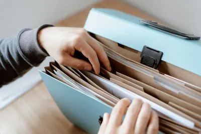 Hands sorting documents in an expanding file folder, preparing to file accounts with Companies House