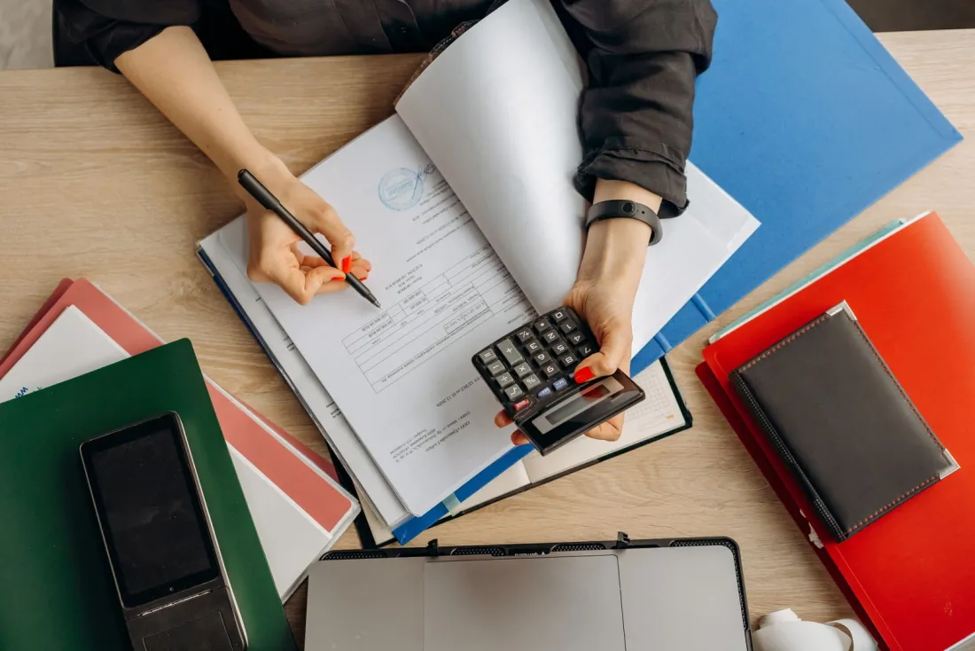 Accountant checking financial documents with a calculator while preparing company accounts for Companies House filing