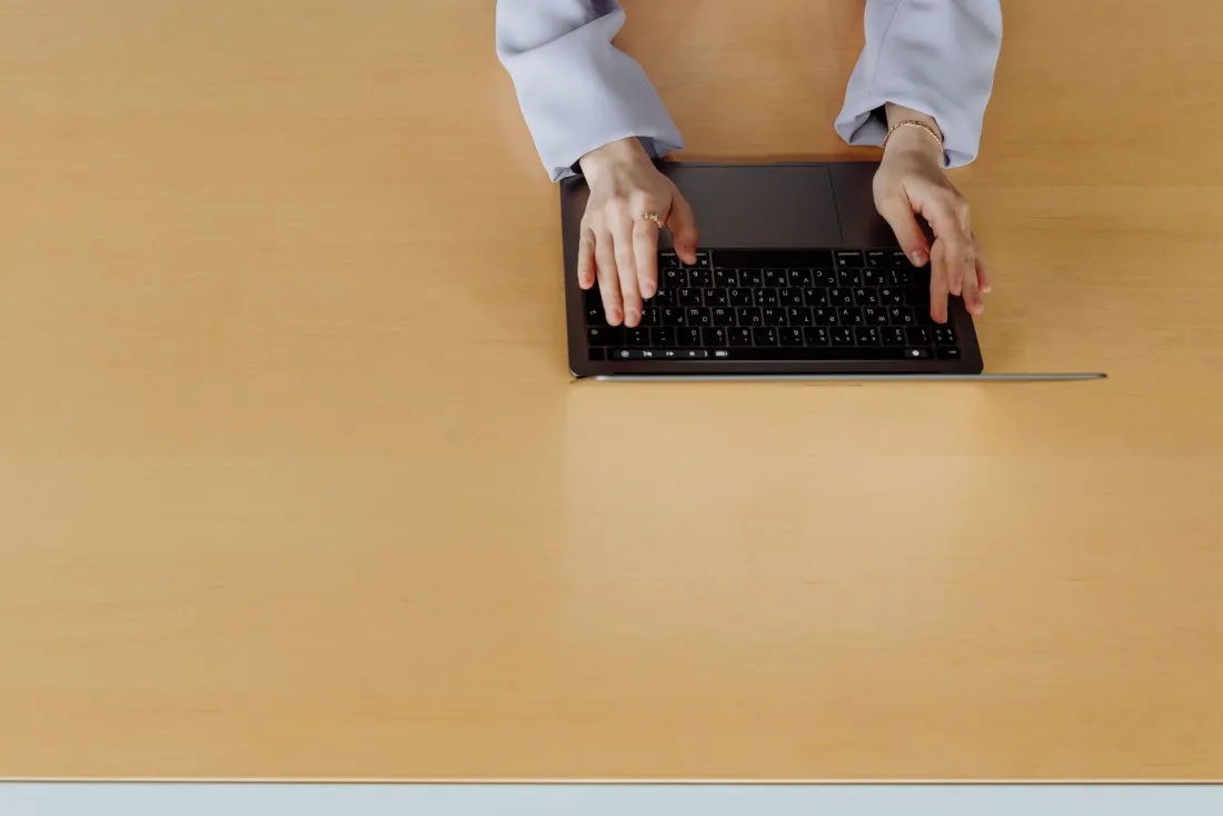 Hands typing on a laptop on a wooden desk, filing accounts with Companies House online through software