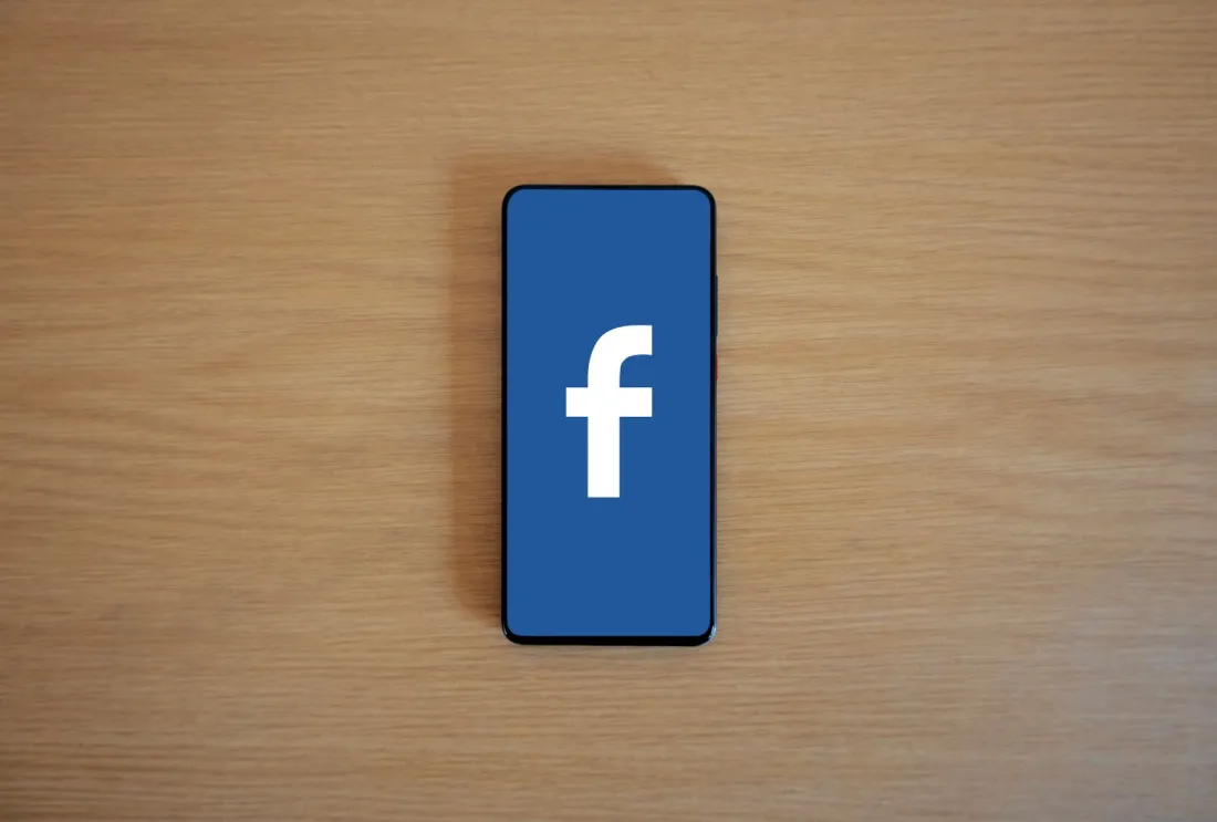 Smartphone showing the Facebook logo on a wooden desk, illustrating what Meta got fined for in New Mexico