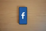 Smartphone showing the Facebook logo on a wooden desk, illustrating what Meta got fined for in New Mexico