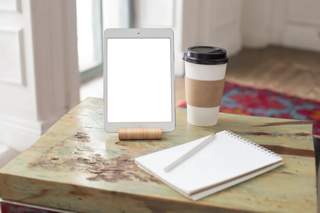 Tablet on a wooden desk beside a coffee and notebook, ready to read the Corporate INTL magazine digital edition