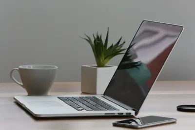 An open laptop beside a coffee mug, potted plant and phone on a desk, illustrating tips for leading teams from home