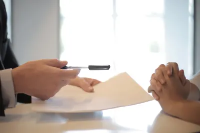 Businessperson handing over a signed document across a table to another person with clasped hands, illustrating rising professional vacancies