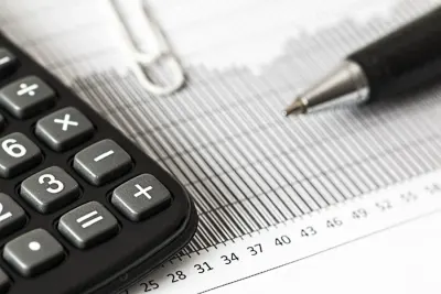 A calculator, paperclip and pen resting on a printed financial ledger, illustrating how tax systems affect multinational companies