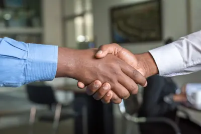 Two businessmen shaking hands in an office setting, illustrating a coopetition strategy between rival firms