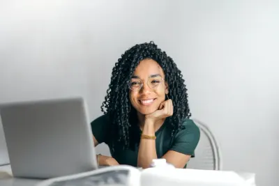 A smiling woman resting her chin on her hand beside an open laptop, illustrating improving employee behaviour