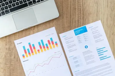 A laptop beside a printed bar chart and a CV on a wooden desk, illustrating today's skills divide in the job market