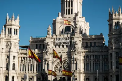 Historic Madrid building displaying a large Refugees Welcome banner beneath Spanish flags