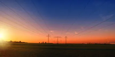 Power lines and pylons crossing a field at sunset, symbolising the energy transition
