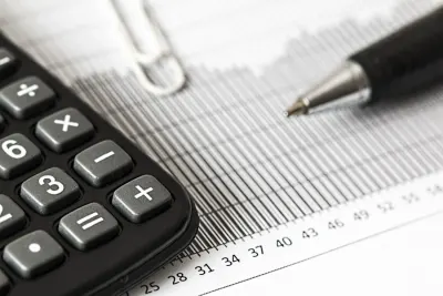 A calculator, paperclip and pen resting on a printed financial ledger, illustrating scrutiny of the auditing profession