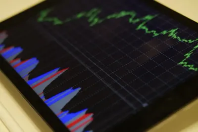 A tablet displaying a financial candlestick chart in green, red and blue, illustrating rising demand for IT professionals in fintech