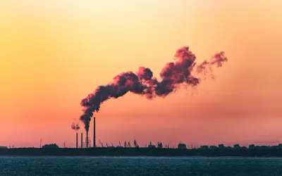 Pink-tinted industrial smoke stacks against a sunset sky, illustrating the net-zero challenge